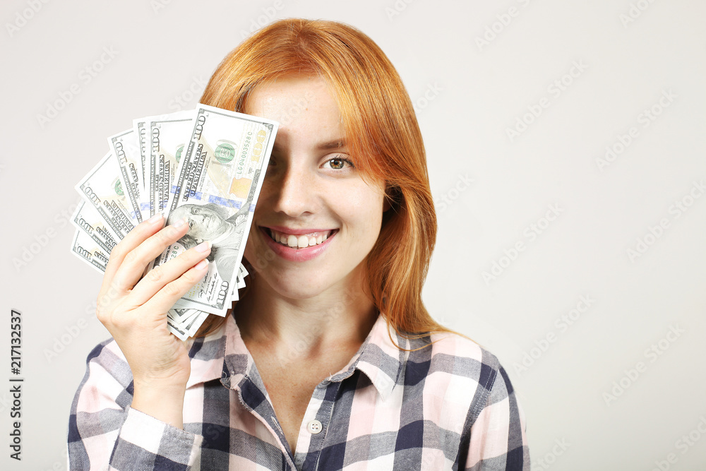 Young beautiful redhead woman covering her face with fistful of money holding bunch of one hundred dollar bills like fan. Excited attractive female with lots of cash. Background, copy space, close up. Young beautiful redhead woman covering her face with fistful of money holding bunch of one hundred dollar bills like fan. Excited attractive female with lots of cash. Background, copy space, close up.