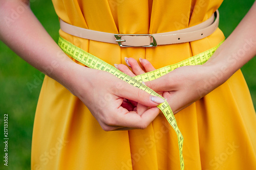 woman dressmaker seamstress measures the body with a measuring tape in a yellow dress with belt in summer park. diet separate food on outdoors