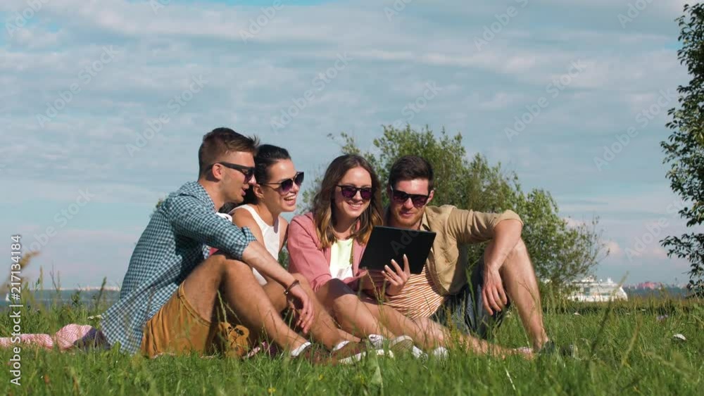 friendship, technology and leisure concept - group of smiling friends with tablet pc computer sitting on grass at summer park in tallinn, estonia friendship, technology and leisure concept - group of smiling friends with tablet pc computer sitting on grass at summer park in tallinn, estonia