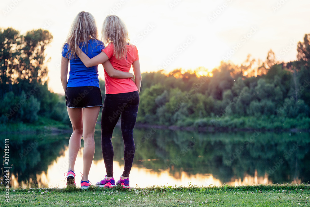 active family at outdoor. two flexibility blonde woman twin sisters in  stylish sportswear enjoy the sunset in the stadium lake sun set background  park Stock Photo | Adobe Stock