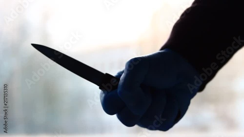 Male holding knife in palm hand in front of scary window light.