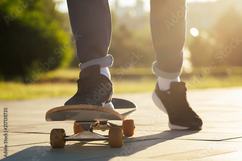 boy skater in a summer park. legs (feet) of man in fashionable jeans and stylish sneakers on a skateboard (longboard) footway asphalt . youth activity skateboarding concept