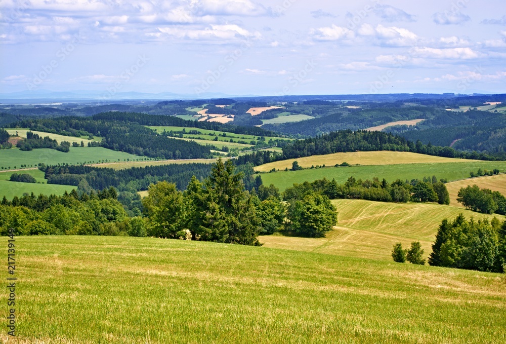 A view of the countryside with meadows, trees, forests and hills under the cloudy sky