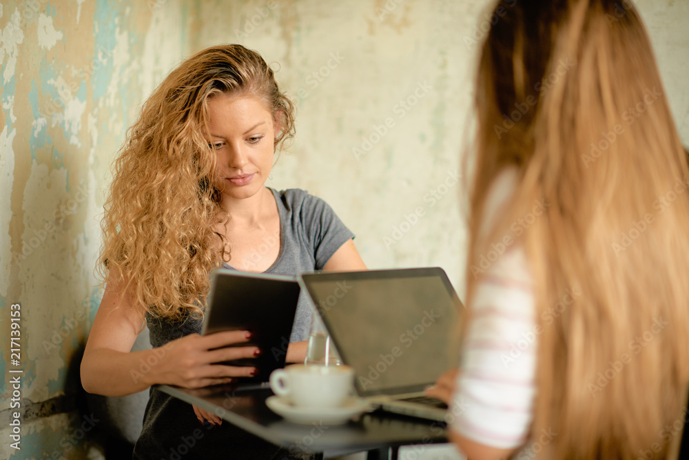 Two women using technologies and drinking coffee while sitting in cafe. Two women using technologies and drinking coffee while sitting in cafe.