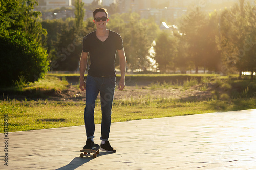 skateboard (longboard) close-up in the hands of a young man in jeans and a black T-shirt in the park