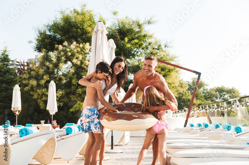 Photo of happy family with kids resting near luxury swimming pool, and having fun with rubber ring outside hotel © Drobot Dean