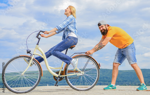 Learn cycling with support. Cycling technique. Woman rides bicycle sky background. How to learn to ride bike as adult. Girl cycling while boyfriend support her. Man helps keep balance and ride bike