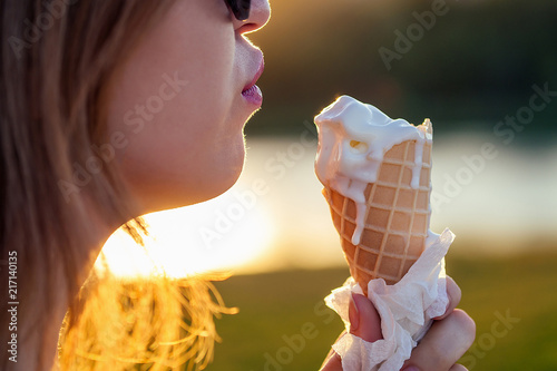 happy californian beautiful woman in sunflasses eat ice cream in a waffle horn cone at sunset on the beach. cool photosession photoshoot of girl on summer park