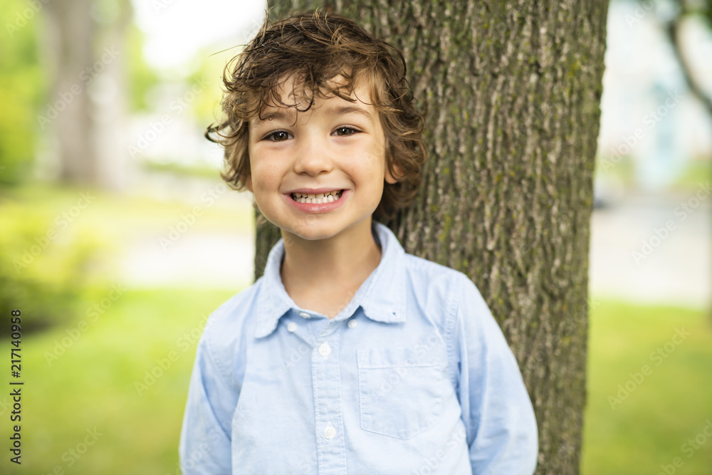 Cute Caucasian boy happily close to a tree