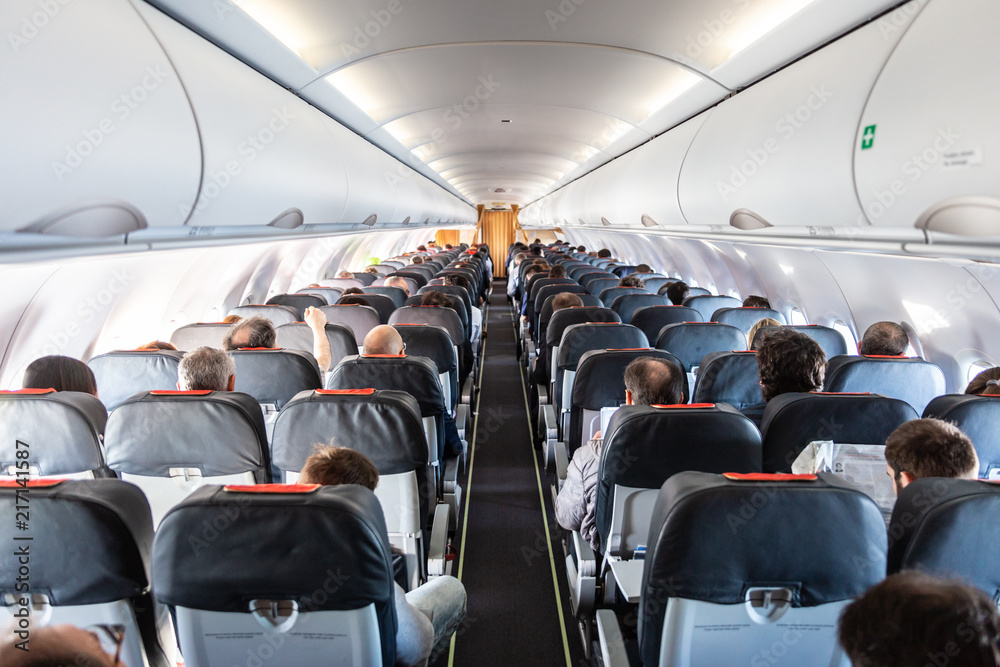 Fototapeta premium Wnętrze samolotu komercyjnego z nie do poznania pasażerami na swoich siedzeniach podczas lotu z tyłu samolotu.