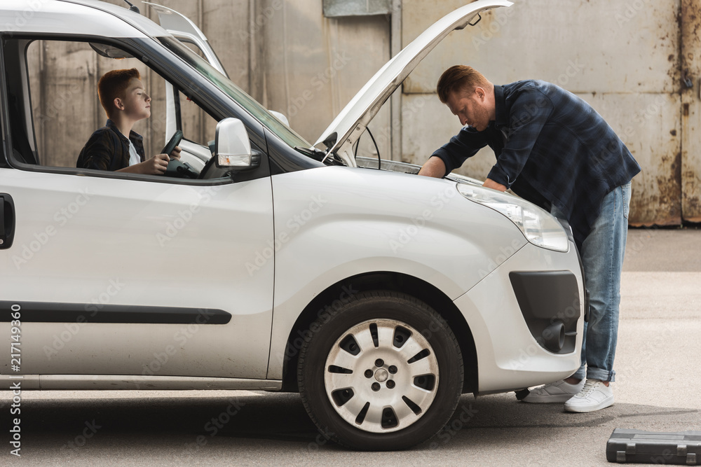 side view of father and son repairing car with open hood side view of father and son repairing car with open hood