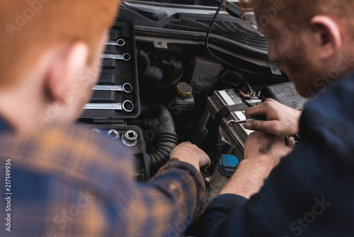 cropped image of father and son repairing car with open hood