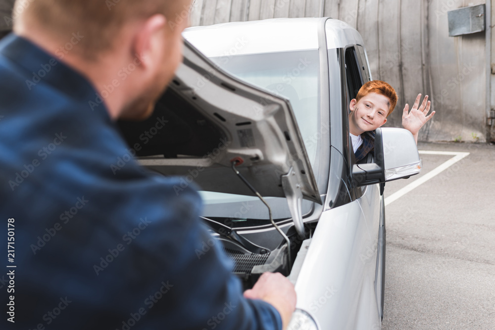 father repairing car with open hood, son waving hand father repairing car with open hood, son waving hand