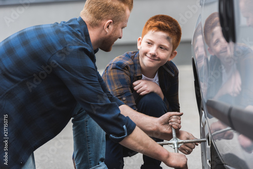 ginger hair father and son changing tire in car with wheel wrench