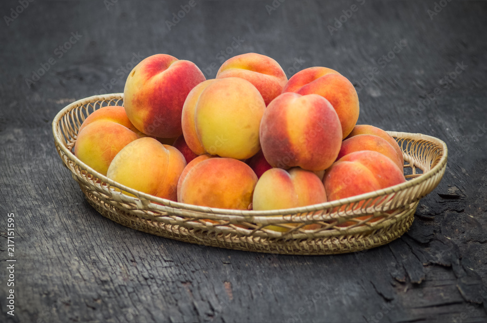 Fresh peaches in wicker basket on dark wood background Fresh peaches in wicker basket on dark wood background