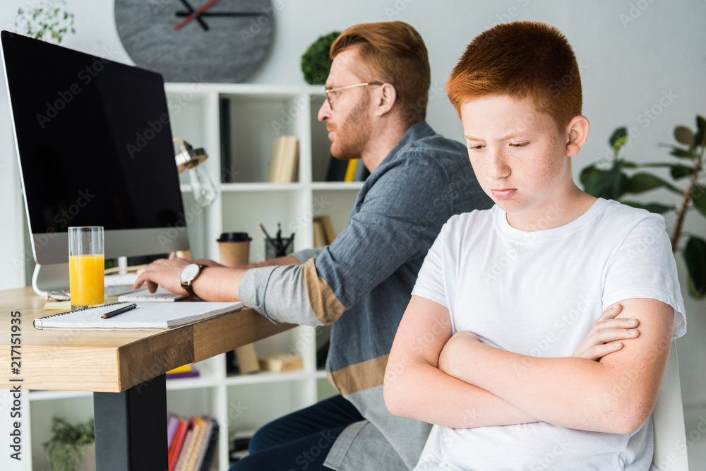 Obraz premium father using computer and sad son looking down at home