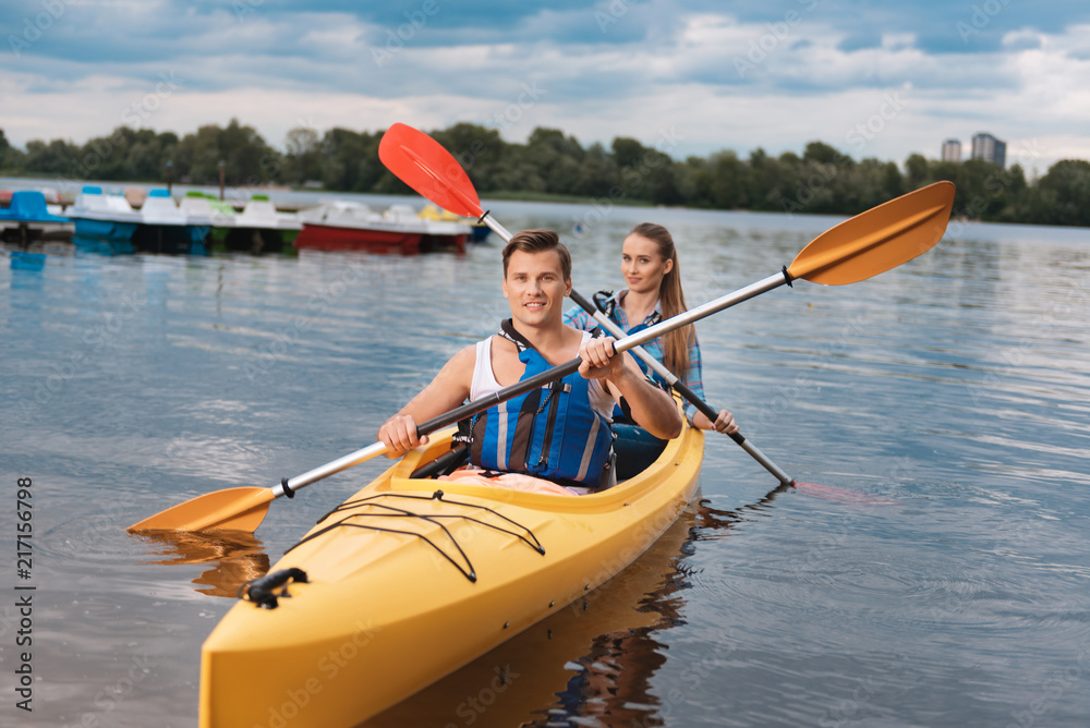 Young athlete. Young handsome blue-eyed athlete training beautiful woman sitting in kayak behind him