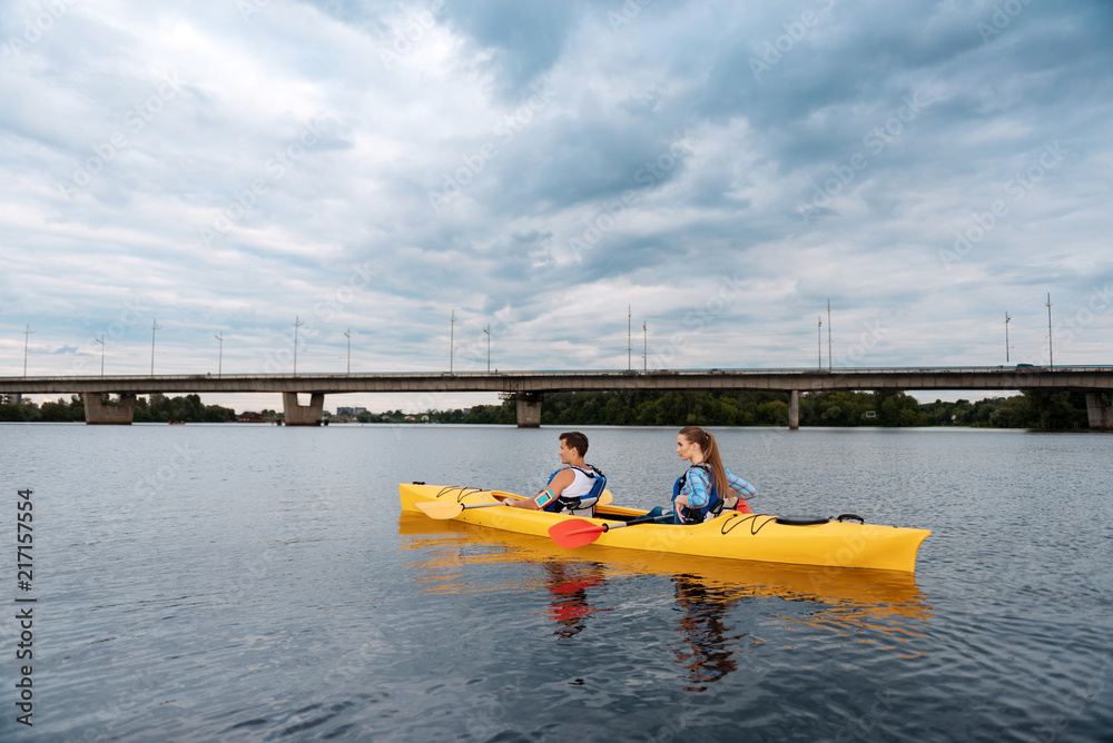Sport couple. Sport active couple holding red and yellow paddles feeling nice while rowing in canoe Sport couple. Sport active couple holding red and yellow paddles feeling nice while rowing in canoe
