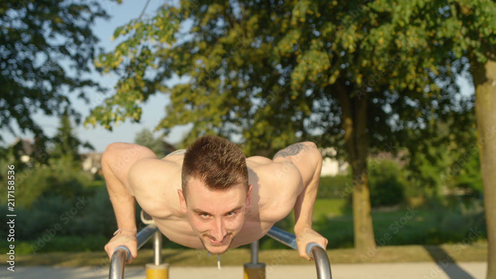 PORTRAIT: Young sportsman having fun doing press ups on parallel bars in park PORTRAIT: Young sportsman having fun doing press ups on parallel bars in park