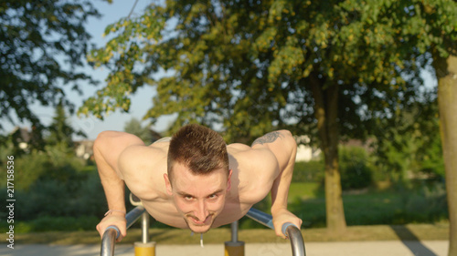 PORTRAIT: Young sportsman having fun doing press ups on parallel bars in park