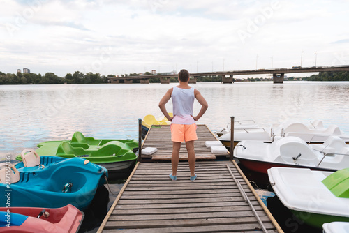 Near river. Good-looking muscle man wearing white shirt and orange shorts standing near river