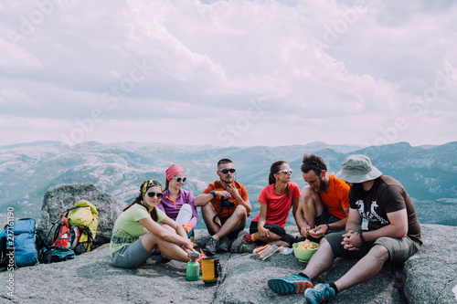 People friendship hangout traveling destination camping concept. Group of six hungry hikers travelers in sportswear relaxing and having snacks after hiking at top of mountain.