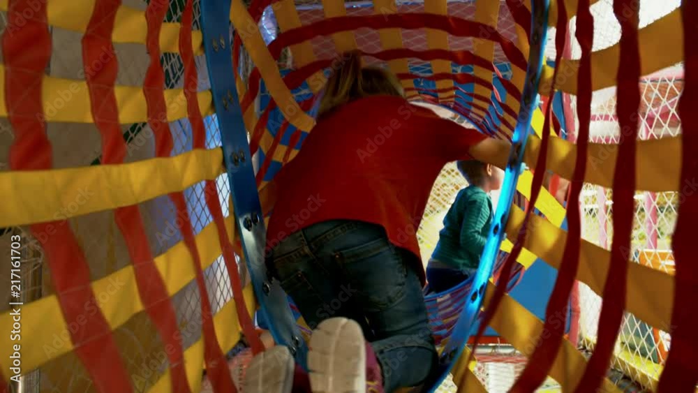 Rear view of two young children of primary school age climbing horizontally through net tunnel in children play center Rear view of two young children of primary school age climbing horizontally through net tunnel in children play center