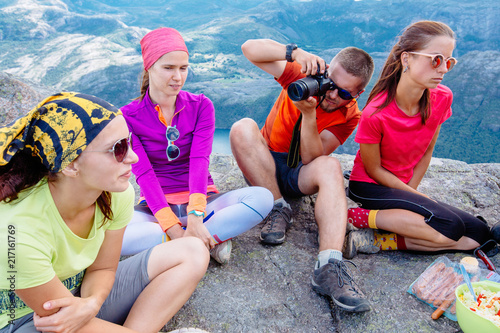 People friendship traveling destination camping concept. Group sportive of four hungry tired hikers travelers having snacks time after hiking at top of mountain. Photographer making portrait photo.