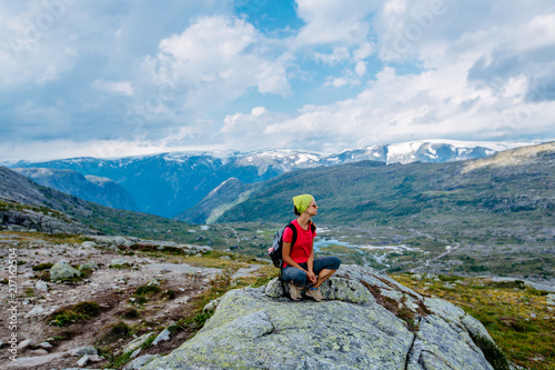 Travel in Norway, woman hiker with backpack sitting on big stone and enjoying scandinavian summer view.