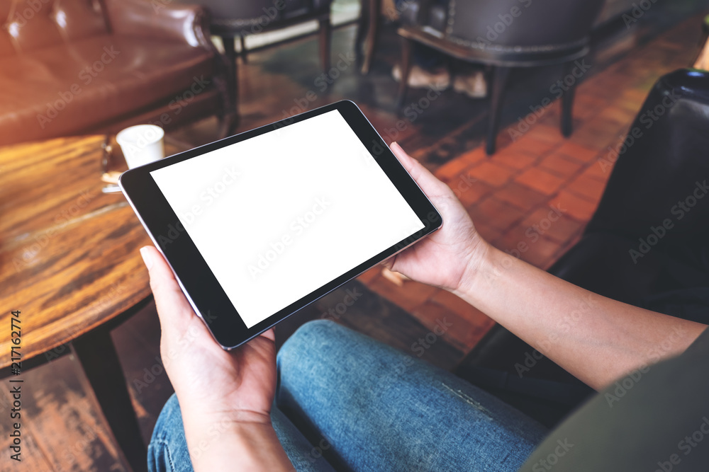 Mockup image of woman's hands holding black tablet pc with blank desktop screen while sitting in cafe