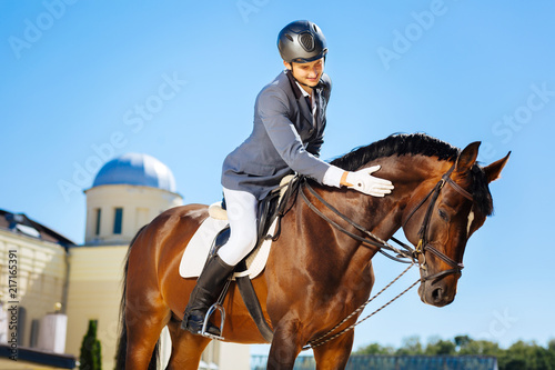 Smiling man. Handsome smiling man wearing helmet and white gloves petting horse while sitting on him