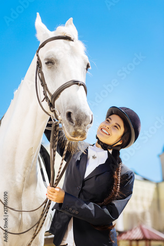 Long braid. Dark-haired female rider with long braid feeling very cheerful while preparing for horse riding