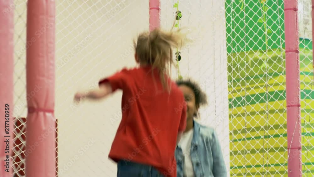Two little girls of different ethnicities smiling and jumping on trampoline together in indoor amusement park Two little girls of different ethnicities smiling and jumping on trampoline together in indoor amusement park