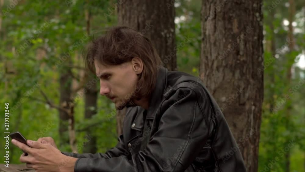 the guy is sitting with the phone in the woods the guy is sitting with the phone in the woods