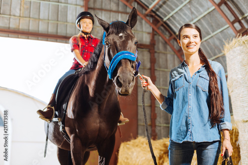 Horse with girl. Professional experienced riding teacher leading horse with blonde-haired beaming girl