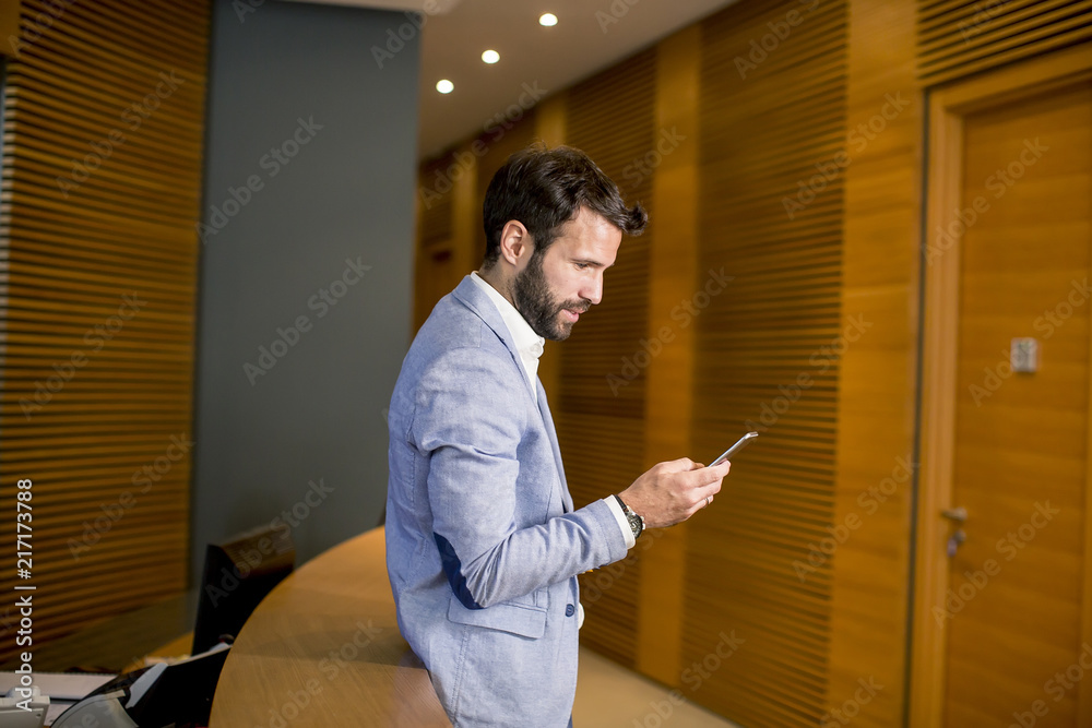 Young businessman standing in office and using mobile phone
