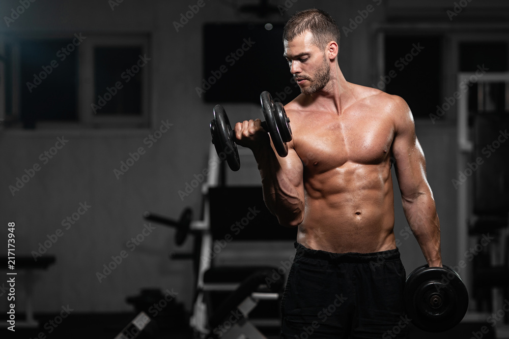 Man trains in the gym. Athletic man trains with dumbbells, pumping his biceps