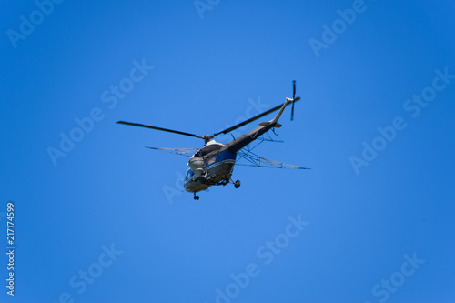 A helicopter of agricultural aviation is flying in the blue sky.