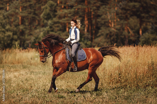 Young woman jockey gallop brown horse strolling across forest.
