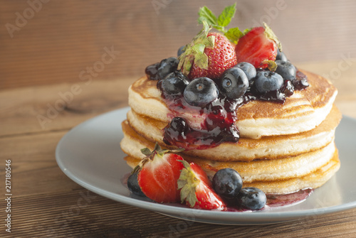 Homemade pancakes or fritters served with strawberry and blueberry jam, delicious dessert for breakfast, rustic style, wooden background. Copy space.