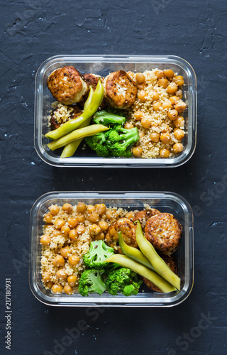 Healthy lunch box - spicy couscous with chickpeas, broccoli, green beans and turkey meatballs on dark background, top view. Copy space