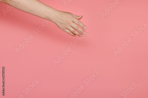 The female hand on a pink background stretches to something diagonally. Copy space.