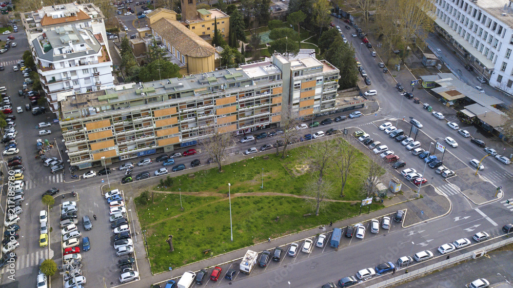 Naklejka premium Aerial view on a small square on the outskirts of a city. In the middle of the square, trees, greenery and parking cars.