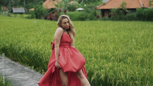 A sexy woman dancer in a red dress and a long knee-length skirt dances, wriggles her body, gracefully moves her arms and wags her head. Emotional and impulsive dance in nature surrounded by greenery photo