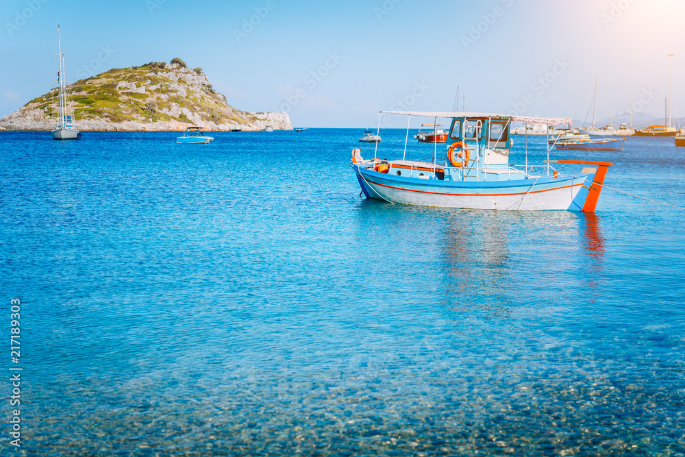 Colorful greek fishing boat at the calm clear water on early summer morning. White rock at the background