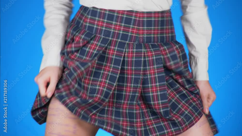 Midsection of teenage girl, cheat sheet written on hips hidden under a skirt. 4k, close-up, blue background, slow-motion shooting.