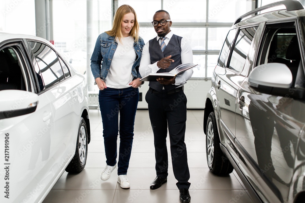 Φωτογραφία African sales consultant helps the girl to choose a new car in the showroom