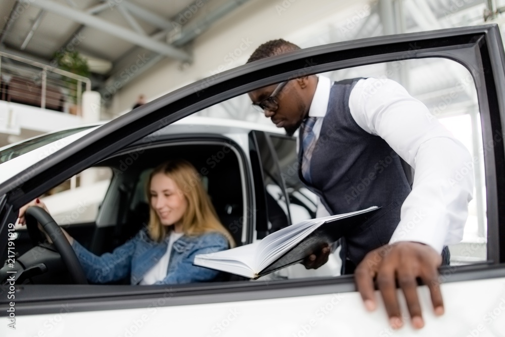African sales consultant shows the girl the salon of a new car in the showroom