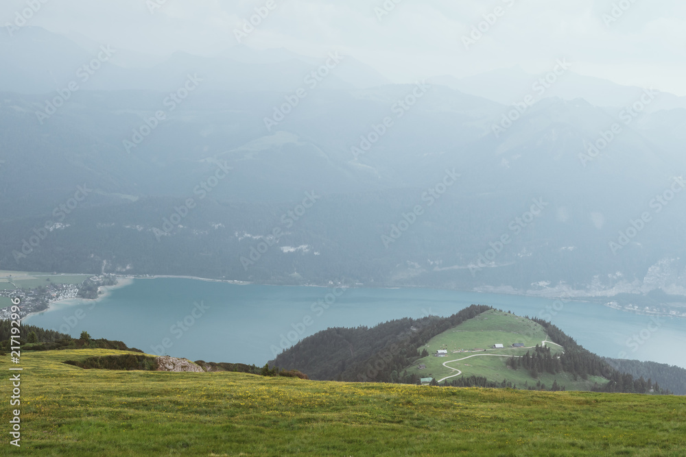 View from top of a mountain in austria with clouds on the sky and mountains in the background - obrazy, fototapety, plakaty 
