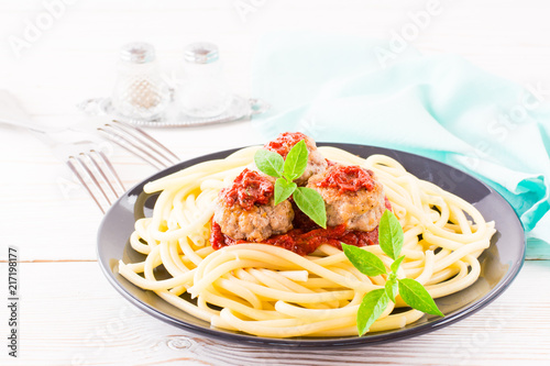 Spaghetti and meatballs in tomato sauce with fresh basil leaves on a plate